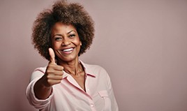 Woman in pink shirt in front of mauve background smiling and giving a thumb’s up