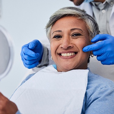 Woman smiling while holding mirror with dentist