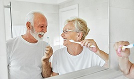 Senior couple smiling while brushing their teeth together in bathroom